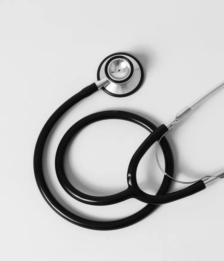 A black stethoscope lies on a white surface. It is partially coiled, showing the metal chest piece and earpieces.