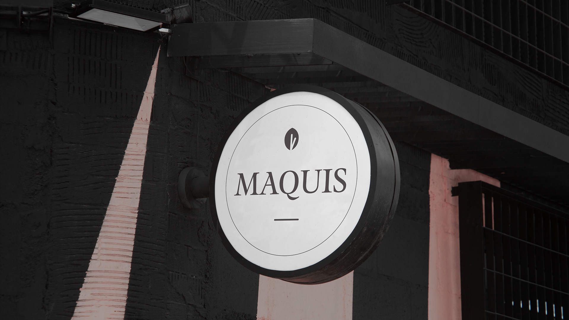 Das runde Ladenschild des Maquis mit schwarzem Logo auf weißem Grund.