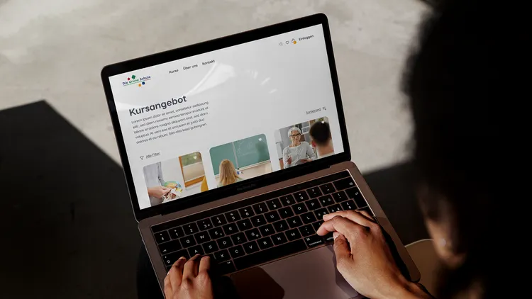 A person is typing on a laptop displaying a webpage titled 'Kursangebot' (Course Offering). The screen shows small images of course activities and text.