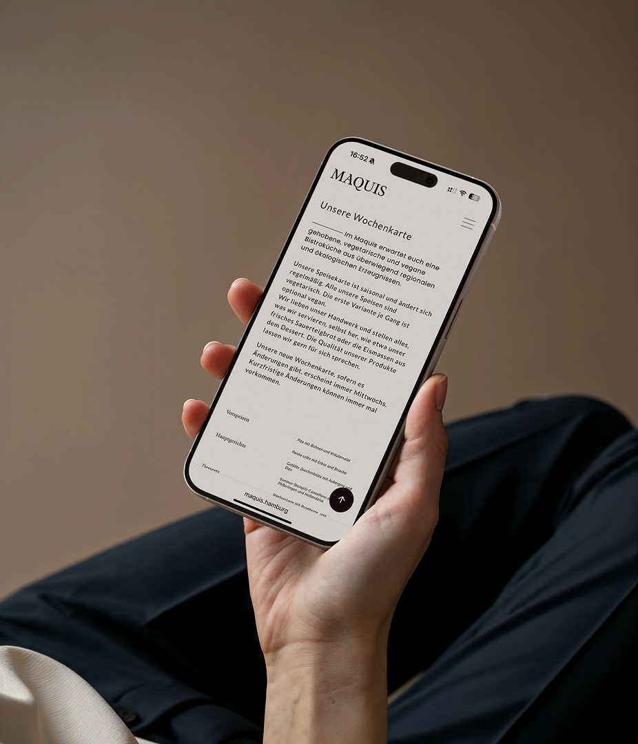 Eine Hand hält ein iPhone, auf dem die Wochenkarte auf der Maquis Website zu sehen ist.