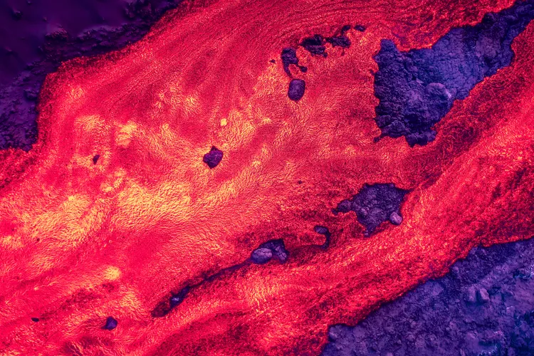 Nahaufnahme von glühender roter Lava, die über dunkles erkaltetes Gestein fließt.