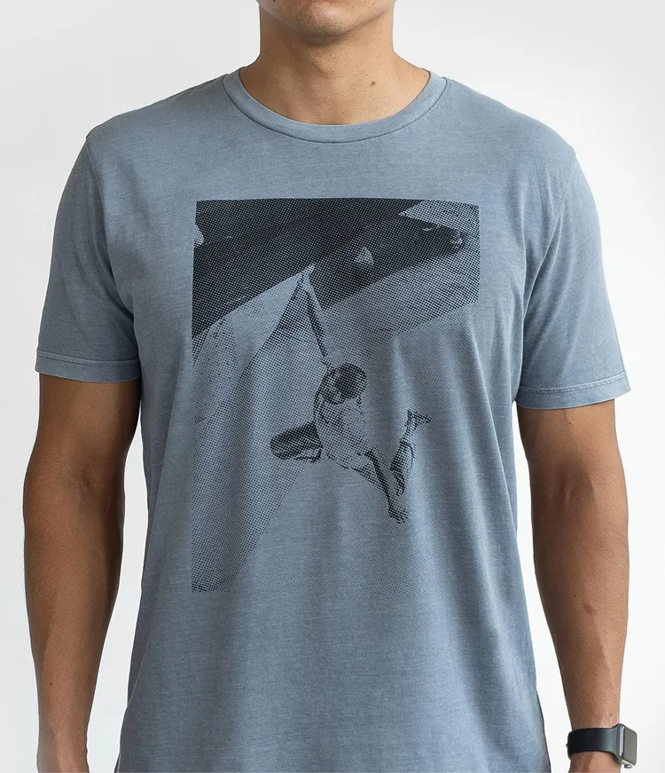 Person wearing a light blue T-shirt with a black and white print of a climber hanging on a wall.
