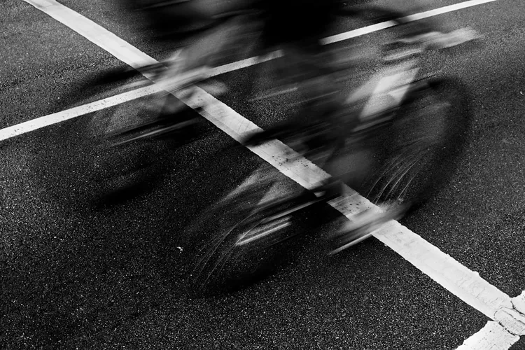Black and white photo of cyclists crossing an intersection with a blurred effect.